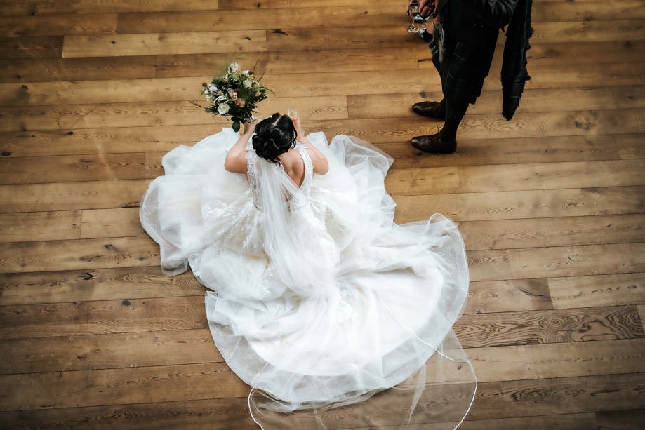 View from above of bride holding bouquet and sitting on wooden floor